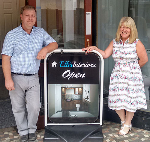 A photo of owners David and Jane stood outside the showroom entrance either side of their advertisement board on a sunny day.